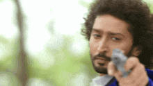 a man with curly hair and a beard is pointing a gun .