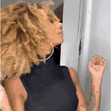 a woman with curly hair is wearing a black tank top and earrings .