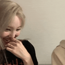 a woman with blonde hair is laughing and covering her mouth with her hands .
