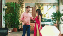 a man and a woman are standing in front of a house . the woman is wearing a red dress .