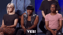 a group of people are sitting in a row and one of them is sitting in front of a group of people and saying yes .
