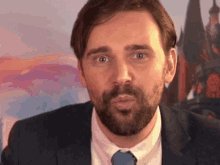 a man with a beard in a suit and tie looks at the camera