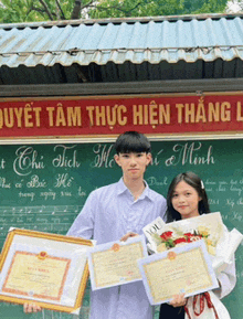 a boy and a girl are holding certificates in front of a sign that says quyet tam thục hien thang l