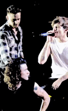 a man in a plaid shirt sings into a microphone while another man looks on