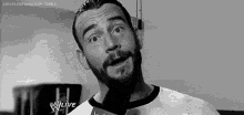 a black and white photo of a man with a beard making a funny face while wearing a white shirt .