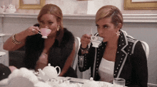 two women sitting at a table drinking tea from cups
