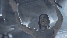 a man without a shirt is singing into a microphone while raising his arms in the air .