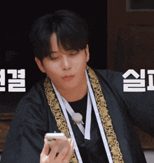 a man wearing a black robe is holding a cell phone with chinese writing behind him