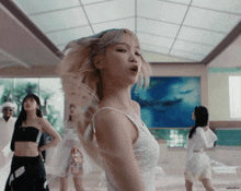 a woman in a white dress is dancing in a room with other women ..