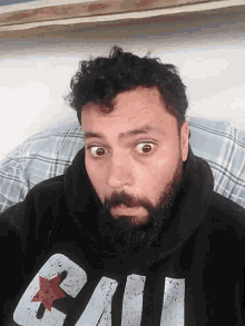 a man with a beard is wearing a black hoodie with the letter u on the front