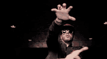 a man wearing sunglasses and a hat with the letter t on it is reaching out his arms