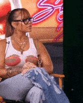 a woman wearing glasses and a tank top that says ' s ' on it sits in a chair