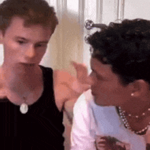 two young men are standing next to each other in a room . one of the men is wearing a necklace .