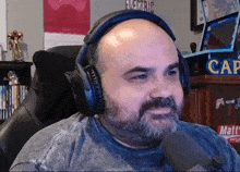 a bald man with a beard wears headphones in front of a sign that says cap on it