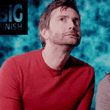 a man in a red shirt is looking up at something .