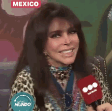 a woman in a leopard print shirt is holding a red microphone and smiling