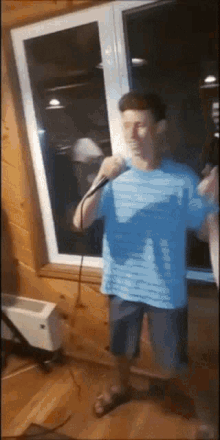 a man in a blue shirt is singing into a microphone in front of a window