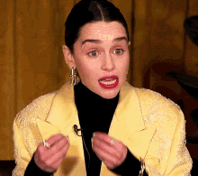 a woman wearing a yellow jacket and black turtleneck is making a face