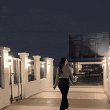 a woman walking down a walkway at night with a fence in the background