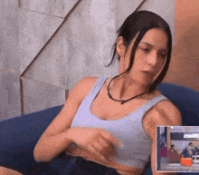 a woman is sitting on a blue couch wearing a crop top and a black necklace .