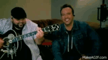 a man is playing a guitar next to another man who is singing into a microphone on makeagif.com
