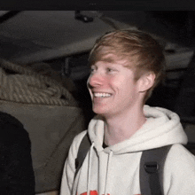 a young man with red hair is smiling and wearing a white hoodie .