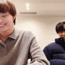 a man in a grey shirt is smiling while another man in a blue jacket looks on