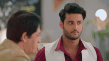 a man in a red shirt and a white vest is talking to another man