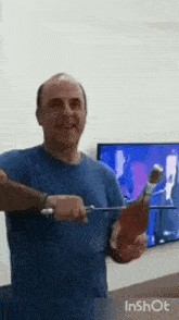 a man in a blue shirt is holding a bottle of wine in front of a tv .