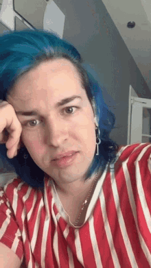 a man with blue hair and a striped shirt is taking a selfie .