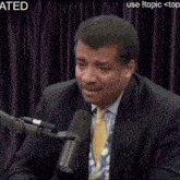 a man in a suit and tie is being spit on by a microphone with the word ated above him