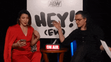 a man and a woman sit in front of a sign that says hey