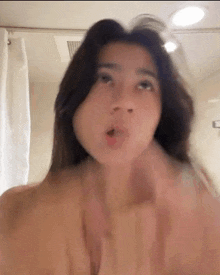 a woman without a shirt is making a funny face in the bathroom .