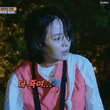 a woman in a pink vest is standing in a dark room with korean writing on the bottom right corner .