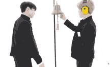a man wearing ear muffs stands next to another man wearing ear muffs and a bell