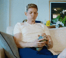 a man is sitting on a couch holding a cup and making a face