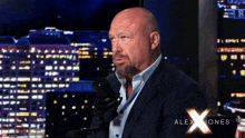 a man in a suit is talking into a microphone with the name alex jones on the bottom of the screen