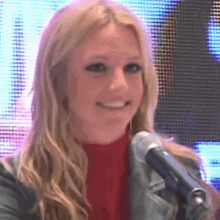 a blonde woman is smiling while holding a microphone in front of a large screen .