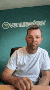 a man sits at a desk in front of a blue wall that says overview view
