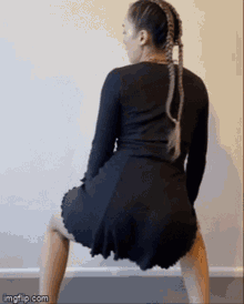 a woman in a black dress is doing a squat in front of a wall ..