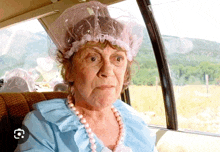 an elderly woman wearing a shower cap and pearls is sitting in the back seat of a car .