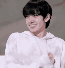 a young man wearing a white hoodie smiles with his arms crossed