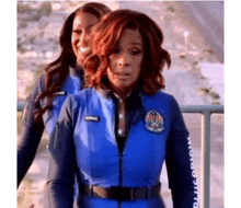 two women are standing next to each other wearing blue jumpsuits .