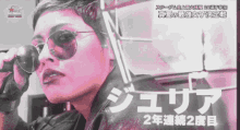 a woman wearing sunglasses and a black jacket stands in front of a sign that says ' nbc ' on it