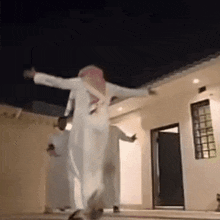 a man in a white robe is dancing in front of a house at night .
