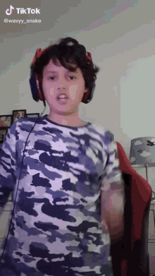 a young boy wearing headphones and a camouflage shirt has a tiktok icon above his head