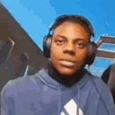 a young man wearing headphones and a blue hoodie looks at the camera .