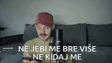 a man sitting on a couch holding a microphone with the words ne jebi me bre vise ne kidaj me written below him