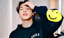 a man wearing a black nomad sweatshirt with a yellow smiley face on the arm