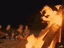 a group of people are sitting around a fire on the beach with the url rbd.gif below them